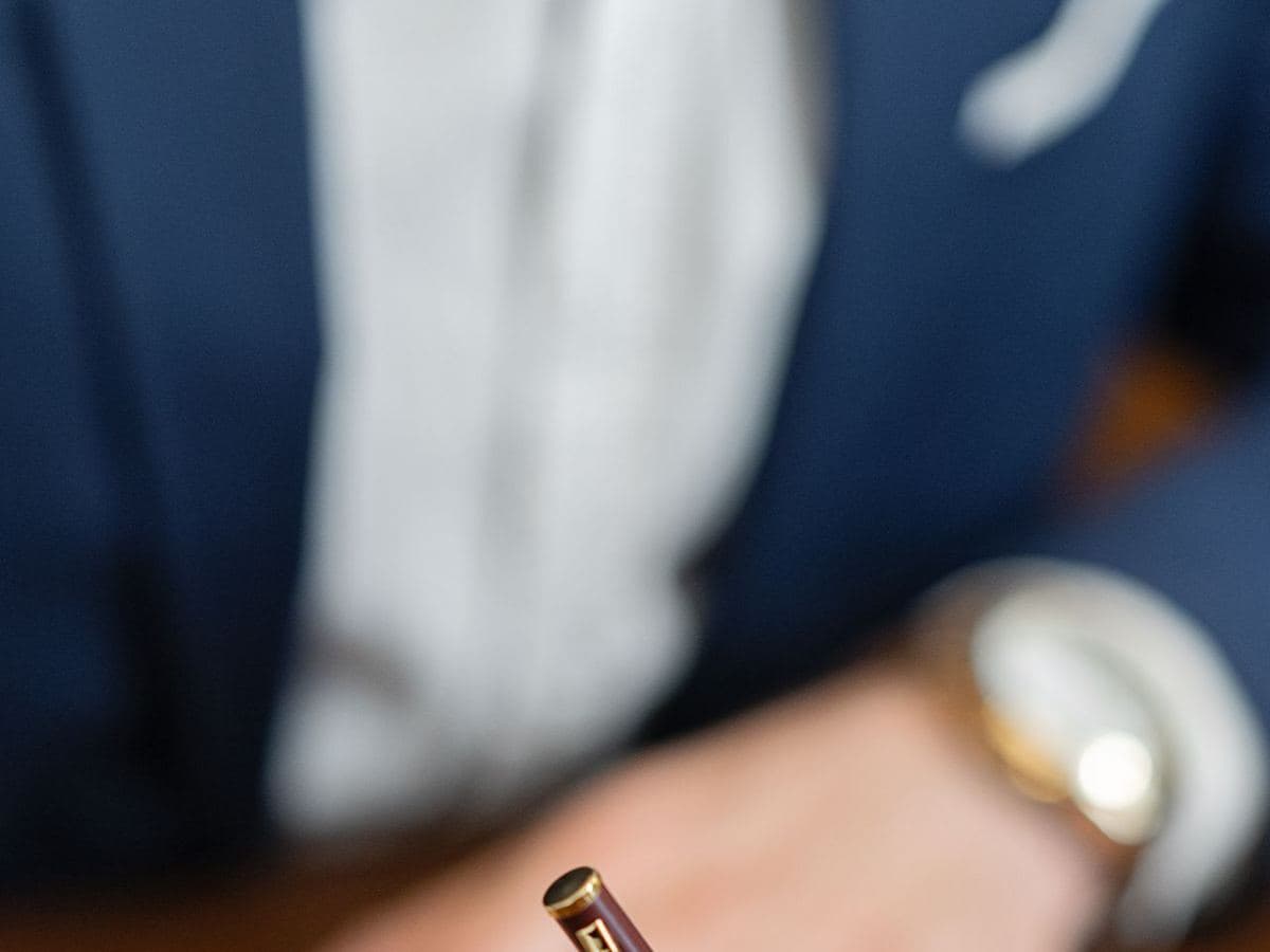 Person in a suit with a watch signing a document at an office desk